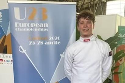 Junger Fechter in weißer Ausrüstung steht neben einem Banner für die U23 Europameisterschaften 2026.