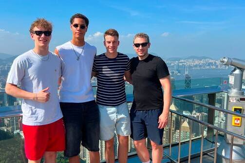 Vier Personen stehen auf einer Aussichtsplattform mit Blick auf die Skyline von Hongkong an einem sonnigen Tag.
