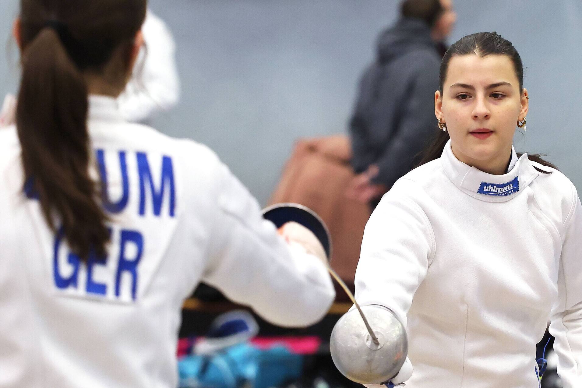 Zwei Fechterinnen in sportlicher Ausrüstung absolvieren ein Training in einer Turnhalle.